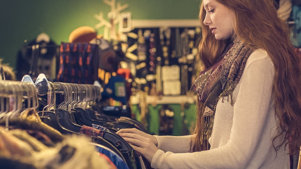 Cliente parcourant un portant de vêtements dans une boutique chaleureuse