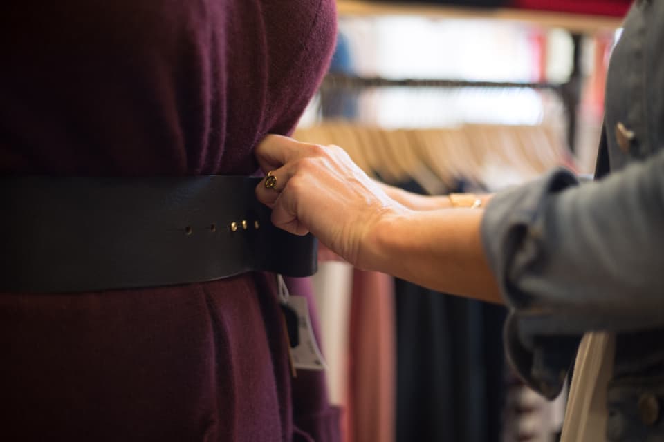 Main ajustant une large ceinture en cuir sur une tenue bordeaux